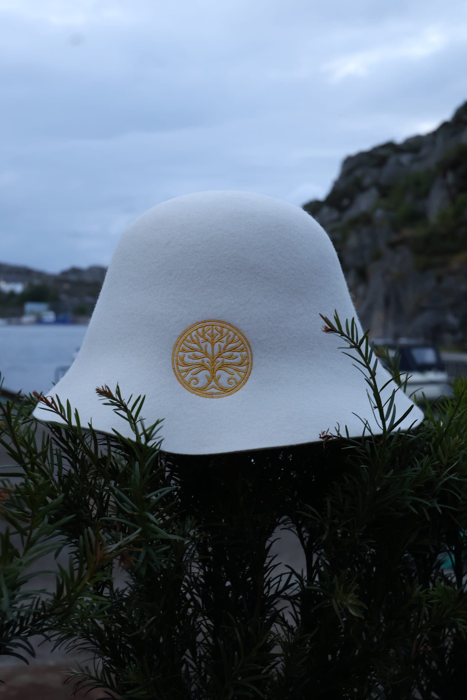 Annonse: hvit badstuehatt med gullbrodert livstre, fjord og fjellside bak.